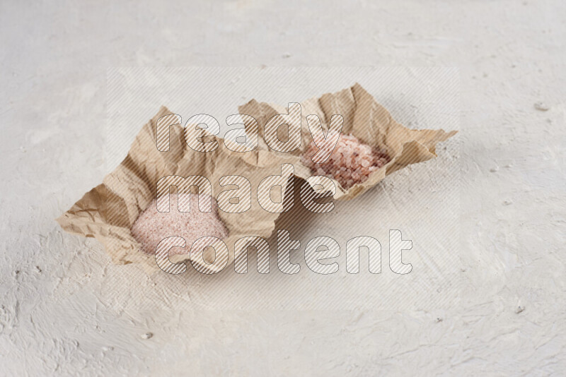 A crumpled piece of paper full of pink himalayan salt on white background
