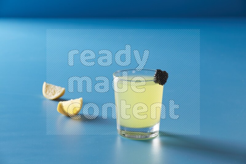 glass of lemon juice with berry on blue background
