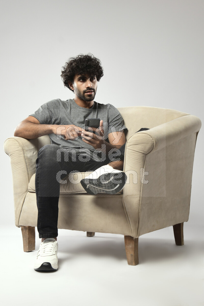 A man wearing casual sitting on a chair browsing on the phone on white background