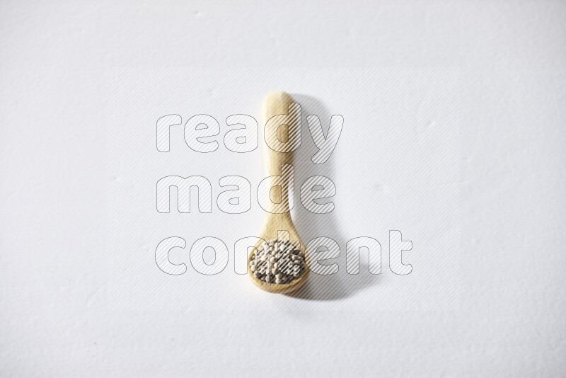 A wooden spoon full of white pepper beads on white flooring