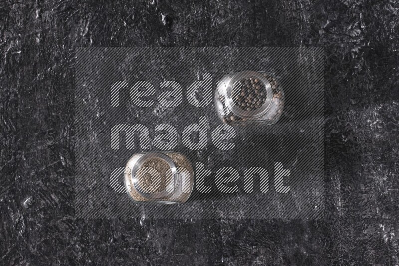 حبوب وبودرة الفلفل الأسود في أوعية زجاجية علي خلفية سوداء