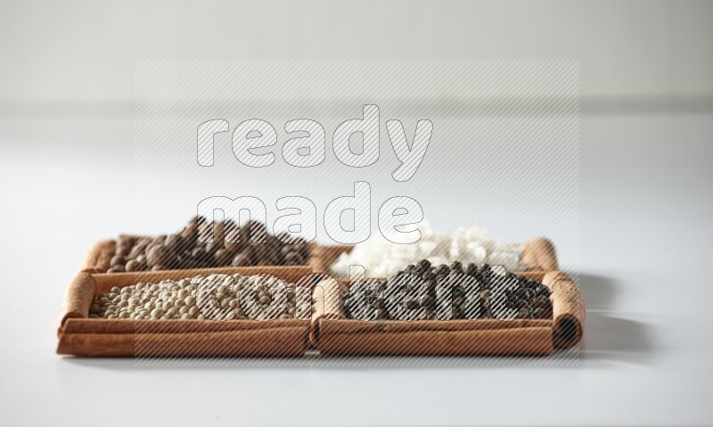 4 مربعات من أعواد القرفة ممتلئة ببهار الفلفل الحلو والملح الأبيض والفلفل الأبيض والفلفل الأسود على أرضية بيضاء