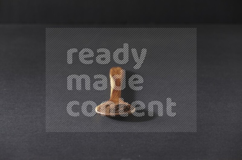 A wooden ladle full of cloves powder on a black flooring