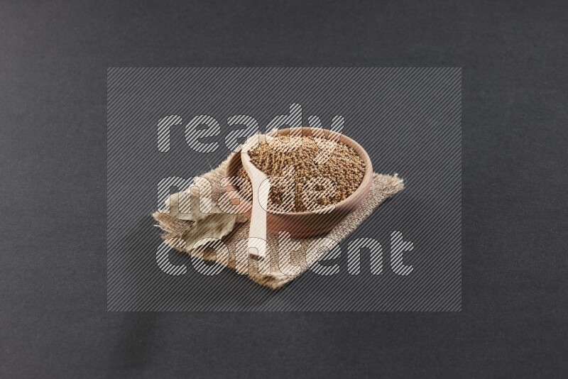 وعاء خشبي ممتلئ ببذور الخردل مع ملعقة خشبية ممتلئة فوق الوعاء علي قطعة من القماش علي خلفية سوداء