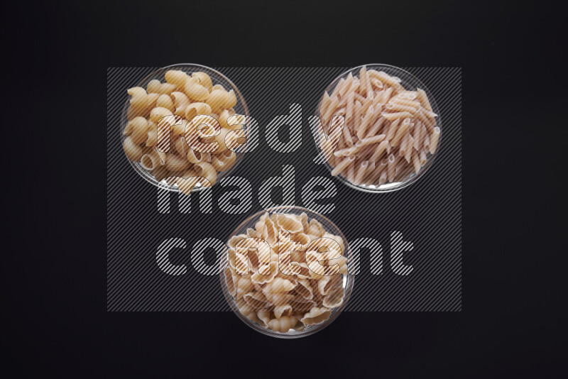 Different pasta types in glass bowls on black background