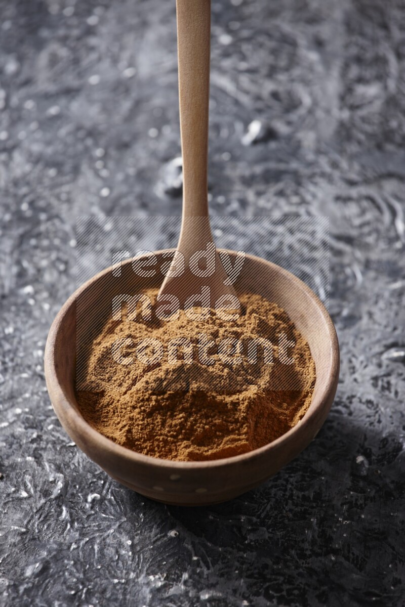 Wooden bowl full of cinnamon powder with a wooden spoon on a textured black background in different angles