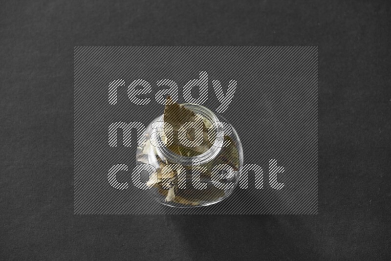 A glass spice jar full of bay laurel leaves on black flooring
