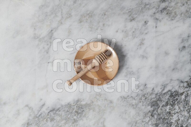 Multicolored pottery plate with wooden honey dipper in it on grey marble background