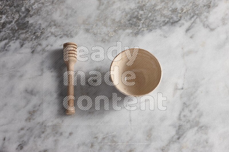 Beige pottery bowl with wooden honey dipper on the side on grey marble background