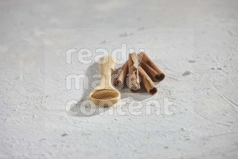 Cinnamon powder in a wooden spoon with cinnamon sticks on white background