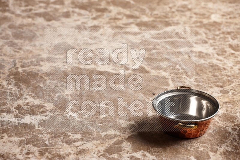A small copper pot on beige marble background