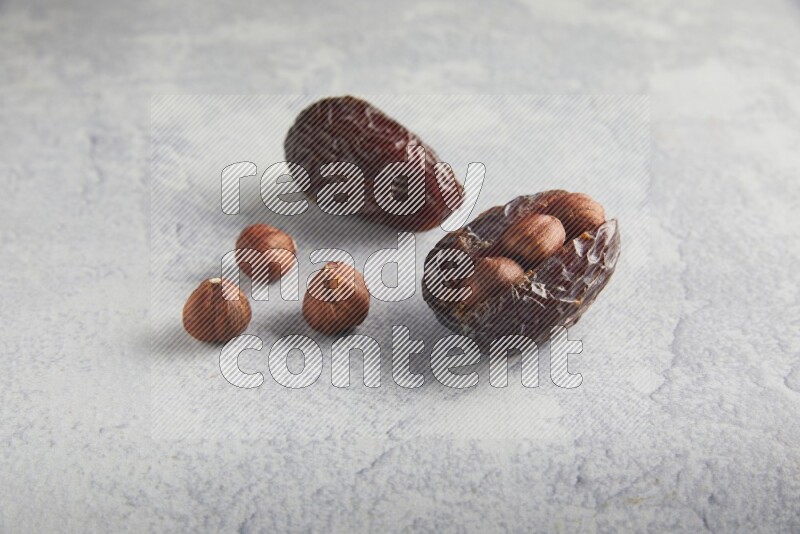 two hazelnuts stuffed madjoul dates on a light grey background