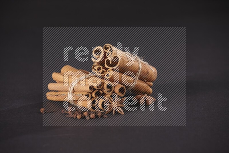 Two bounded stacks of cinnamon sticks with cloves and star anise on black background