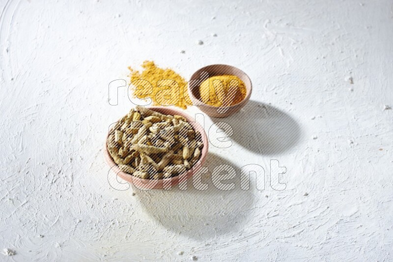 وعاءان خشبيان، أحدهما ممتلئ ببودرة الكركم والآخر بأصابع الكركم المجففة، على خلفية بيضاء