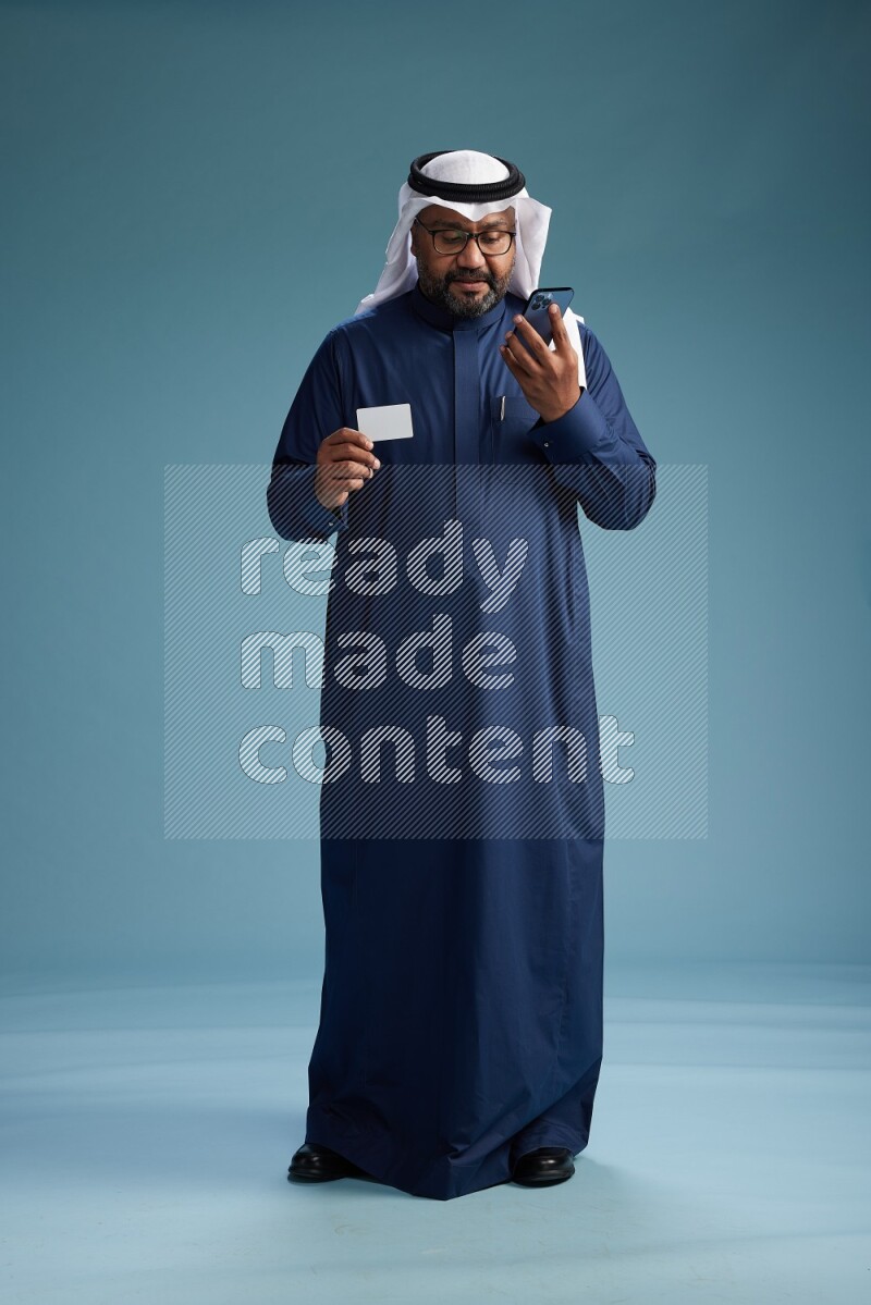 Saudi Man with shimag Standing holding ATM card while talking on phone on blue background