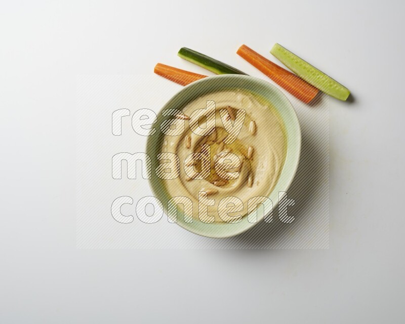 Hummus in a green plate garnished with pine nuts on a white background