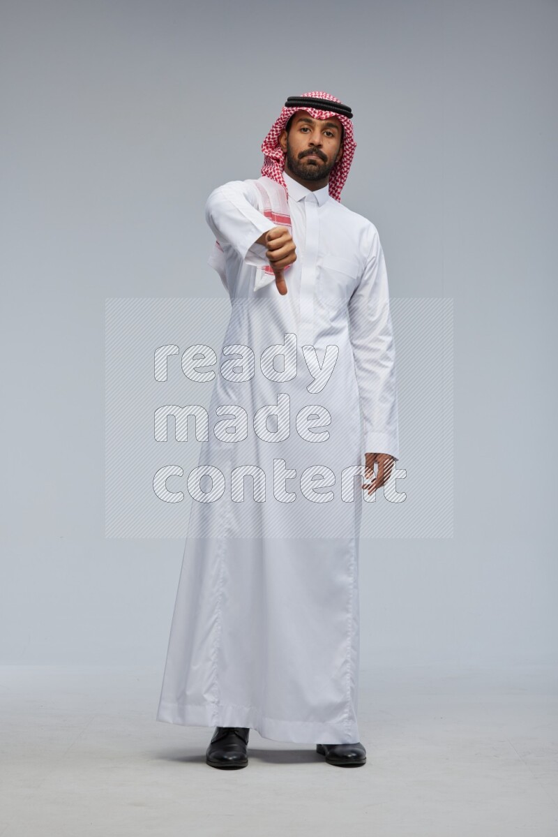 Saudi man Wearing Thob and shomag standing interacting with the camera on Gray background