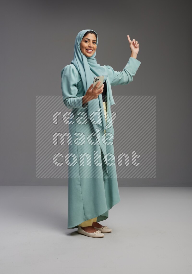 Saudi Woman wearing Abaya standing texting on phone on Gray background