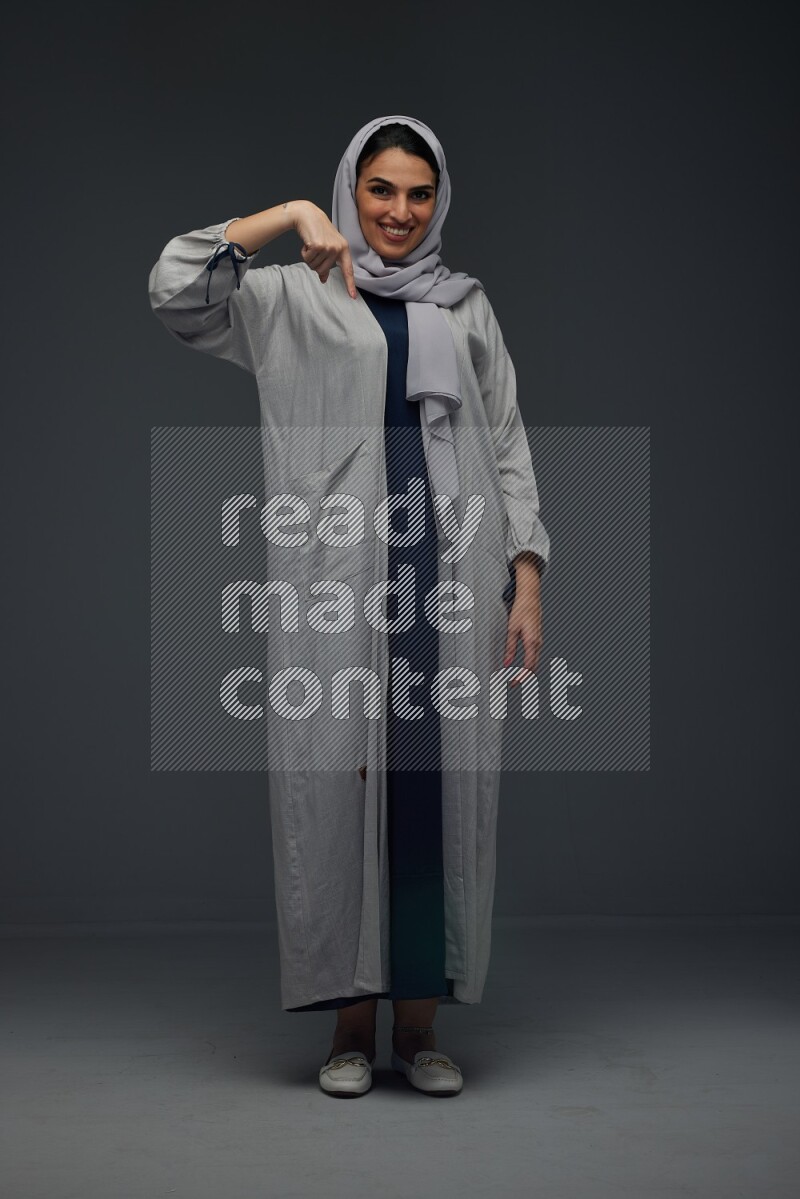 A Saudi woman wearing a light gray Abaya and head scarf standing and making multi poses eye level on a grey background