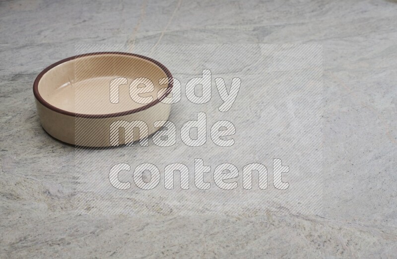 A beige pottery oven bowl on grey marble background