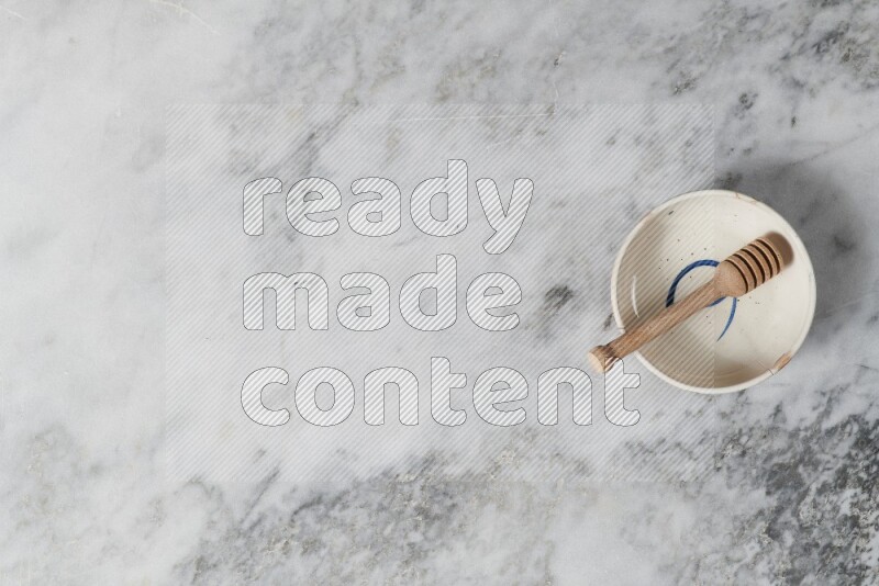 Multicolored pottery bowl with wooden honey dipper in it on grey marble background
