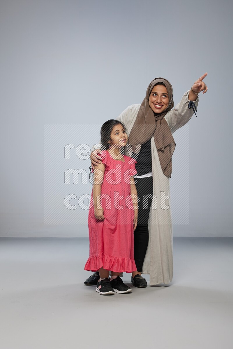 A girl and her mother interacting with the camera on gray background