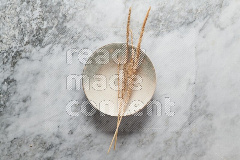 Wheat stalks on multicolored pottery plate on grey marble background