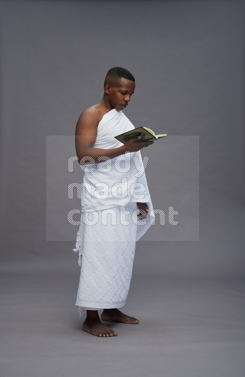 A man wearing Ehram Standing reading quran on gray background
