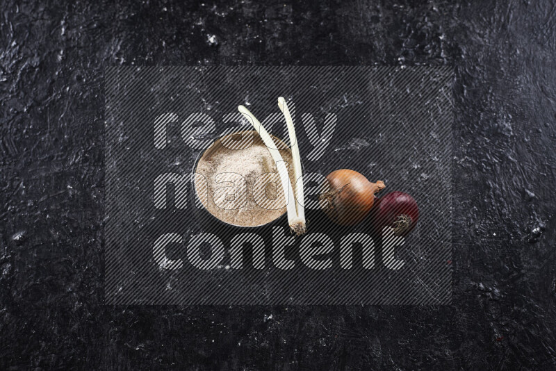A black pottery bowl full of onion powder on black background