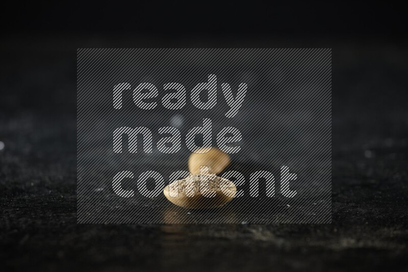 A wooden spoon full of cardamom powder on textured black flooring