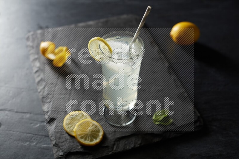 A glass of lemon juice with a straw on black background