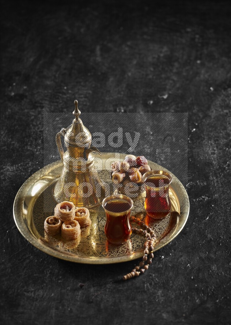 Oriental sweets with dates and a drink on a metal tray in a dark setup
