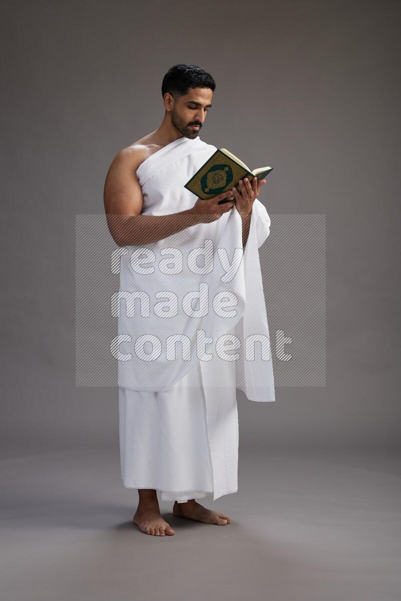 A man wearing Ehram Standing reading quran on gray background