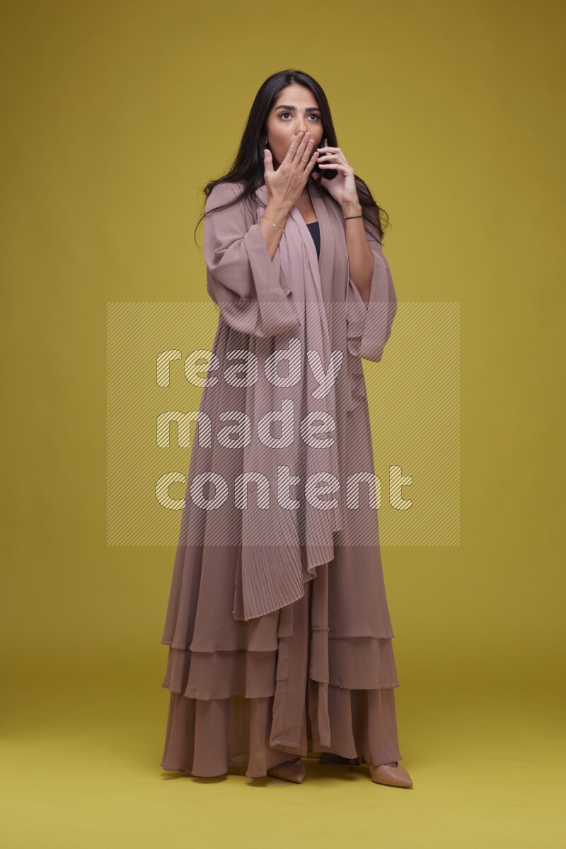 A woman Calling on a Yellow Background wearing Brown Abaya