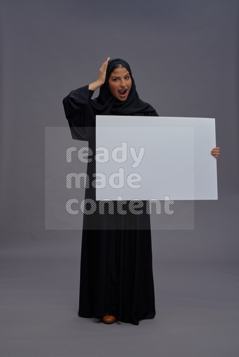 Saudi woman wearing Abaya standing holding white board on gray background