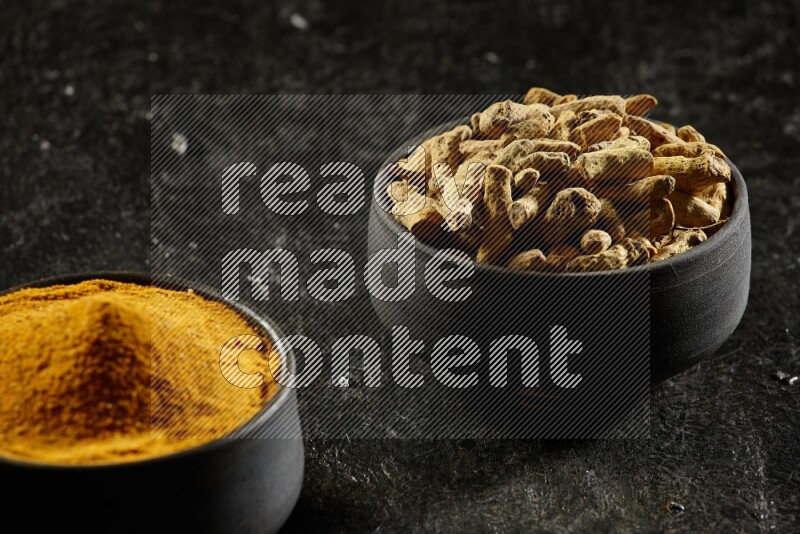 وعاءان من الفخار باللون الأسود، أحدهما ممتلئ ببودرة الكركم والآخر ممتلئ بأصابع كاملة من الكركم المجفف على خلفية سوداء