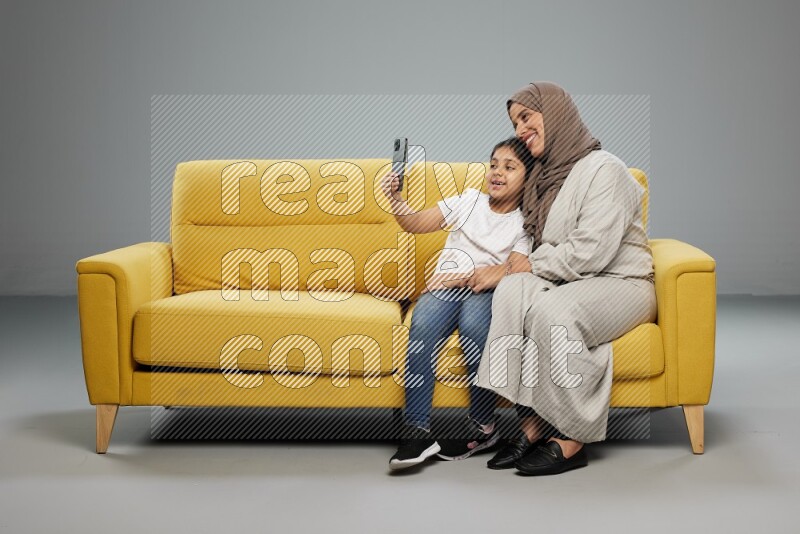 A girl sitting taking selfie with her mother on gray background