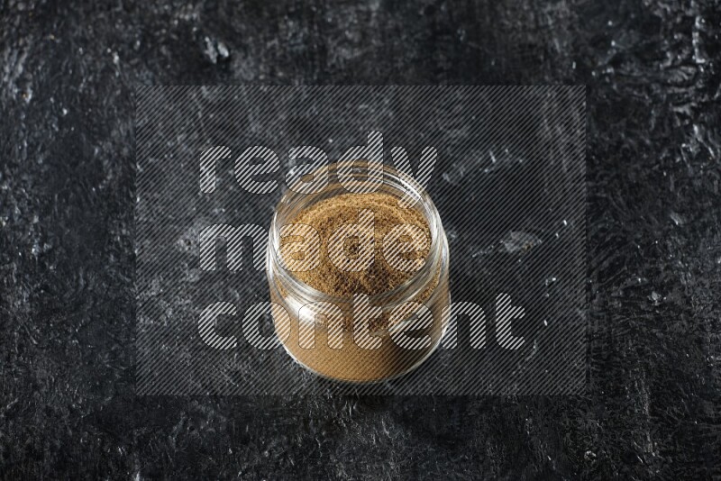 وعاء زجاجي ممتلئ ببودرة الكمون على خلفية سوداء