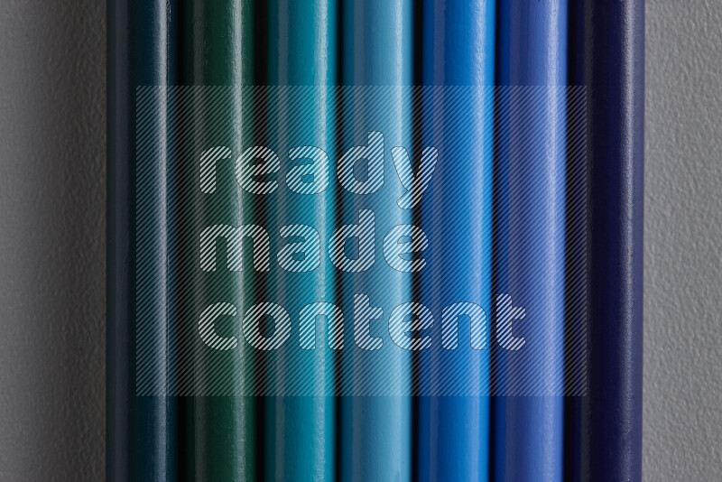 A collection of colored pencils arranged showcasing a gradient of blue hues on grey background