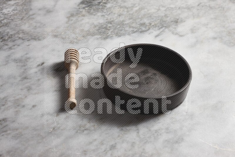 Black pottery oven plate with wooden honey dipper on the side on grey marble background