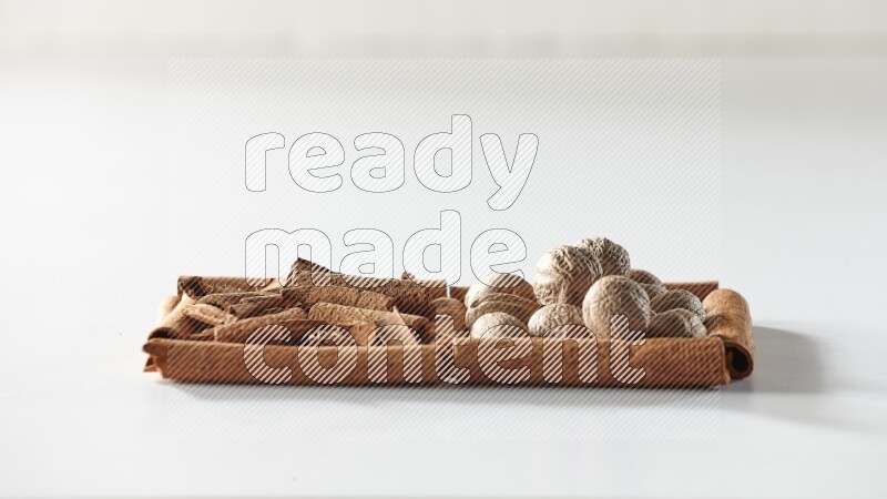 مربعان من أعواد القرفة ممتلئان بقطع من القرفة وجوزة الطيب علي خلفية بيضاء