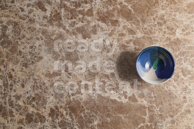 A multicolored pottery bowl on beige marble background