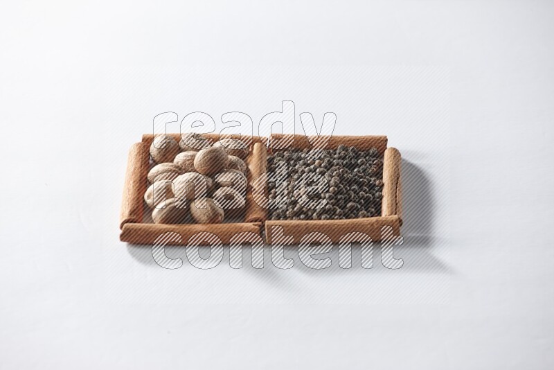 مربعان من أعواد القرفة ممتلئان بحبوب الفلفل الأسود وجوزة الطيب علي خلفية بيضاء