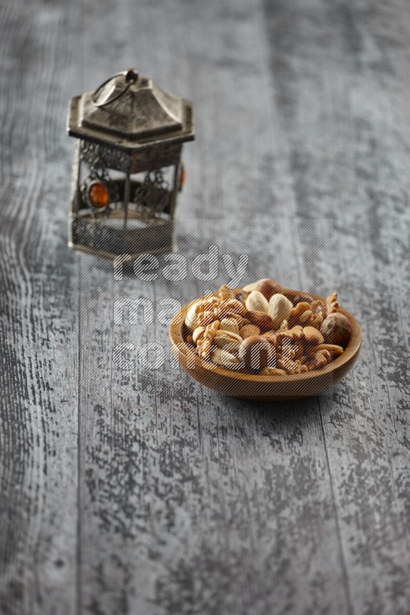 A silver lantern with different drinks, dates, nuts, prayer beads and quran on grey wooden background