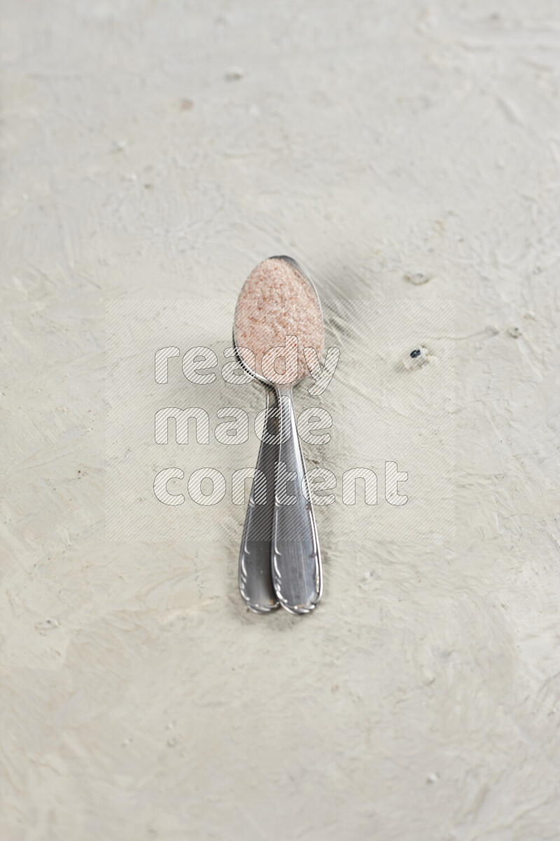 2 metal spoons filled with fine table salt and fine pink himalayan salt on white background