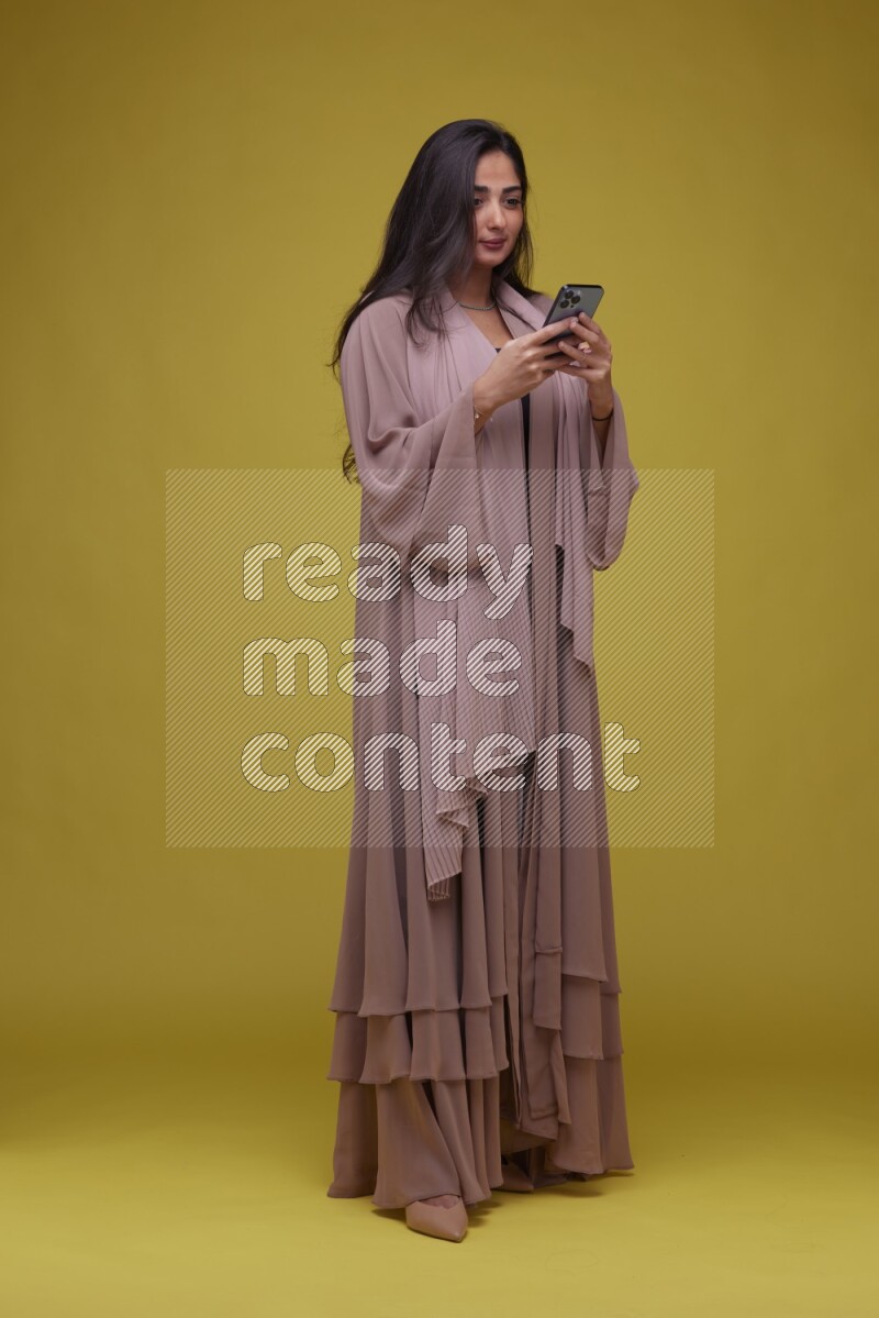A woman Texting on a Yellow Background wearing Brown Abaya