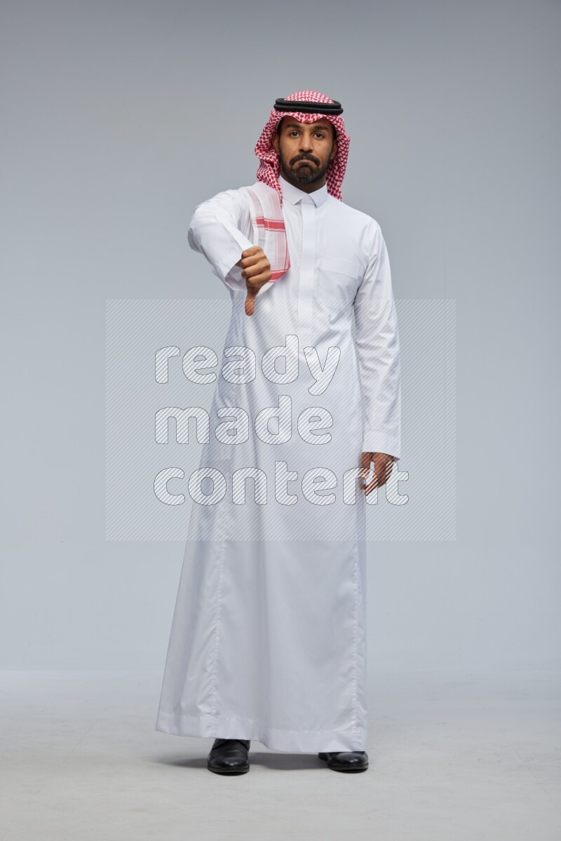 Saudi man Wearing Thob and shomag standing interacting with the camera on Gray background