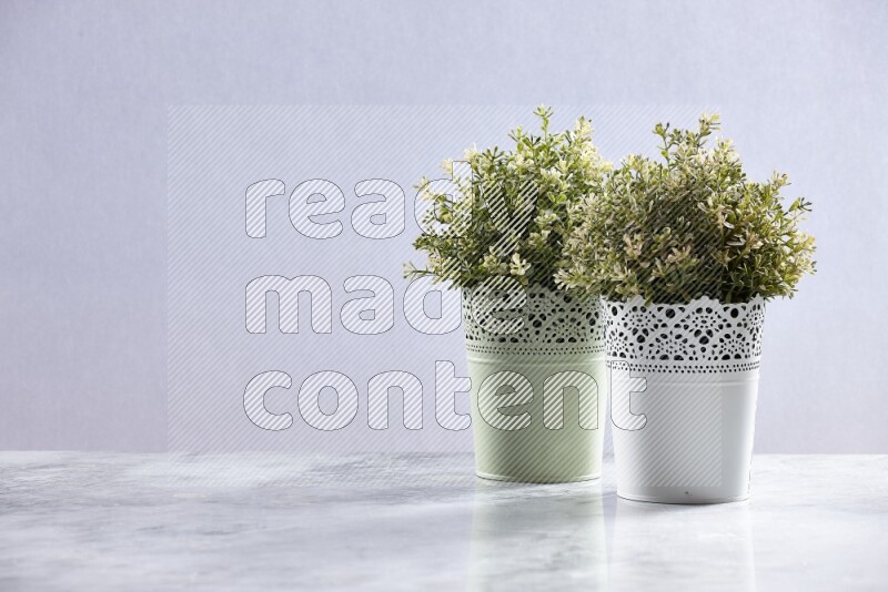 Two different artificial plants in white and green decorative pots on grey marble background