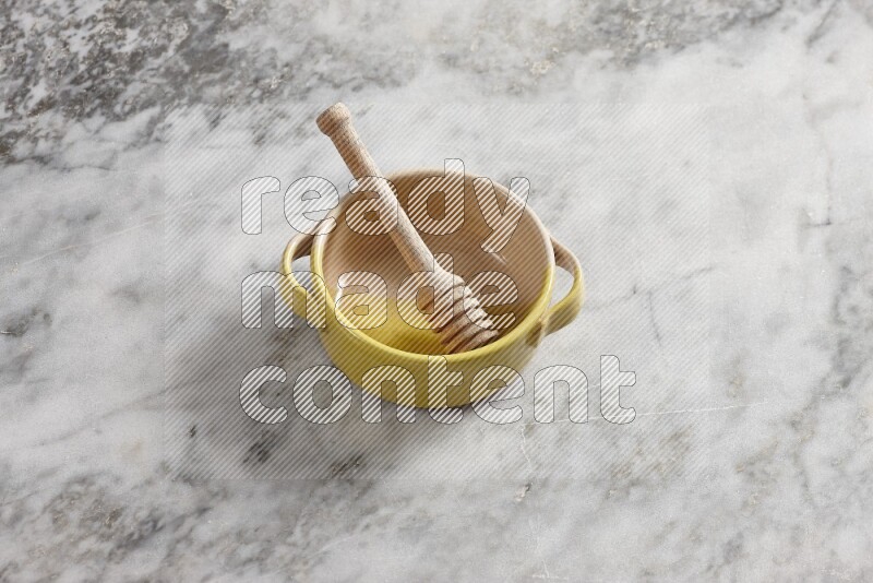 Multicolored pottery bowl with wooden honey dipper in it on grey marble background