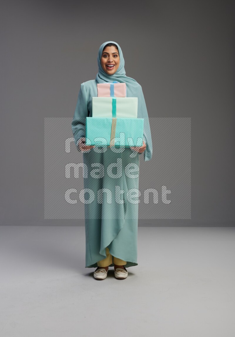 Saudi Woman wearing Abaya standing holding gift box on Gray background